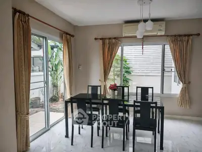 Elegant dining room with glass table, modern chairs, and large windows offering natural light and garden view.