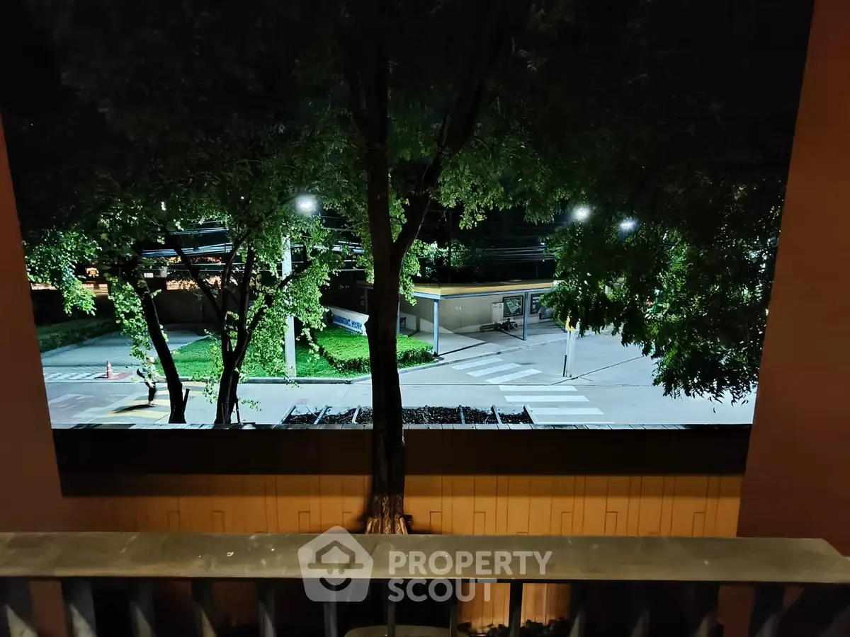 Night view from balcony overlooking street and trees, serene urban setting.