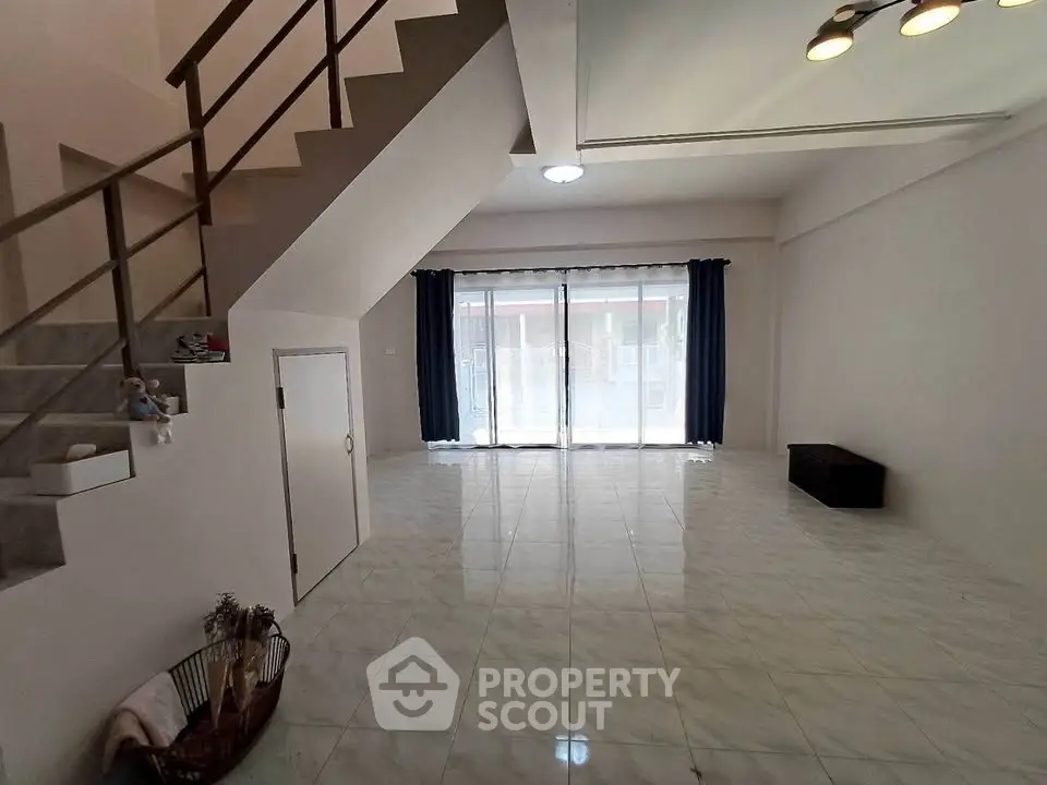 Spacious modern living room with large windows and staircase, perfect for family gatherings.