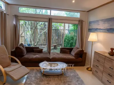 Cozy living room with large windows and garden view, featuring brown sofas and modern decor.