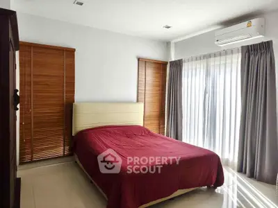 Cozy bedroom with natural light, featuring a red bedspread and modern window treatments.