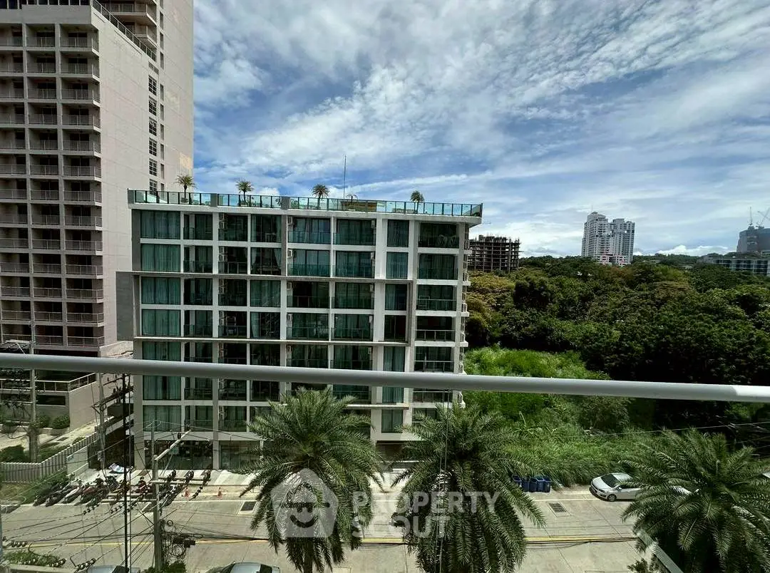 Stunning cityscape view from a high-rise balcony with lush greenery and modern buildings.