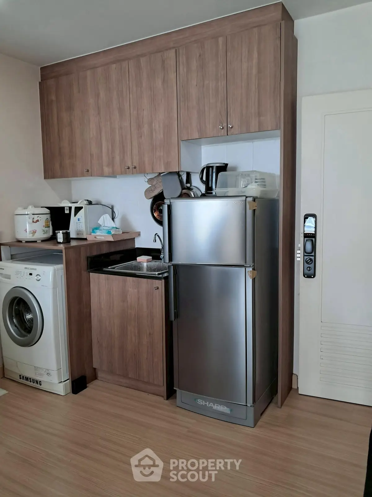 Compact kitchen with modern appliances including fridge, washing machine, and microwave in a cozy apartment.