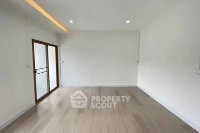 Spacious empty room with wooden flooring and sliding glass door leading to balcony.