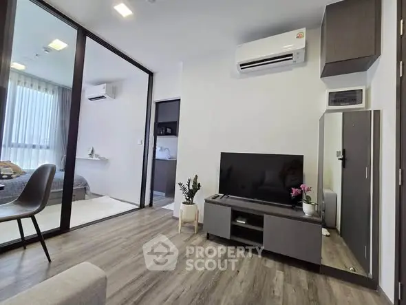 Modern living room with sleek design and large TV, adjacent to a cozy bedroom with natural light.