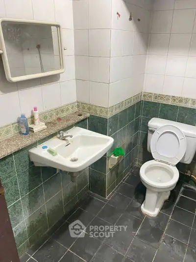 Basic bathroom with sink, toilet, and mirror in tiled setting.