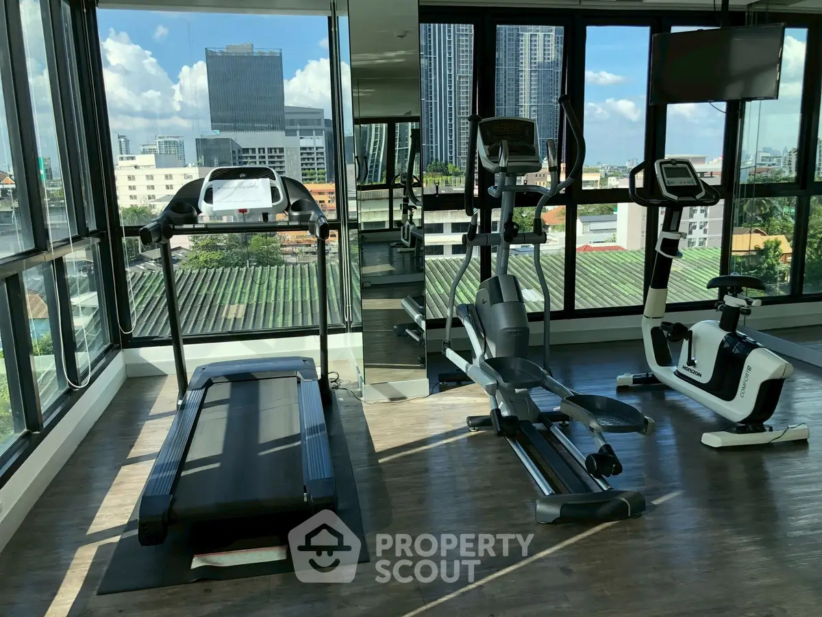 Modern gym with city view and exercise equipment in high-rise building.