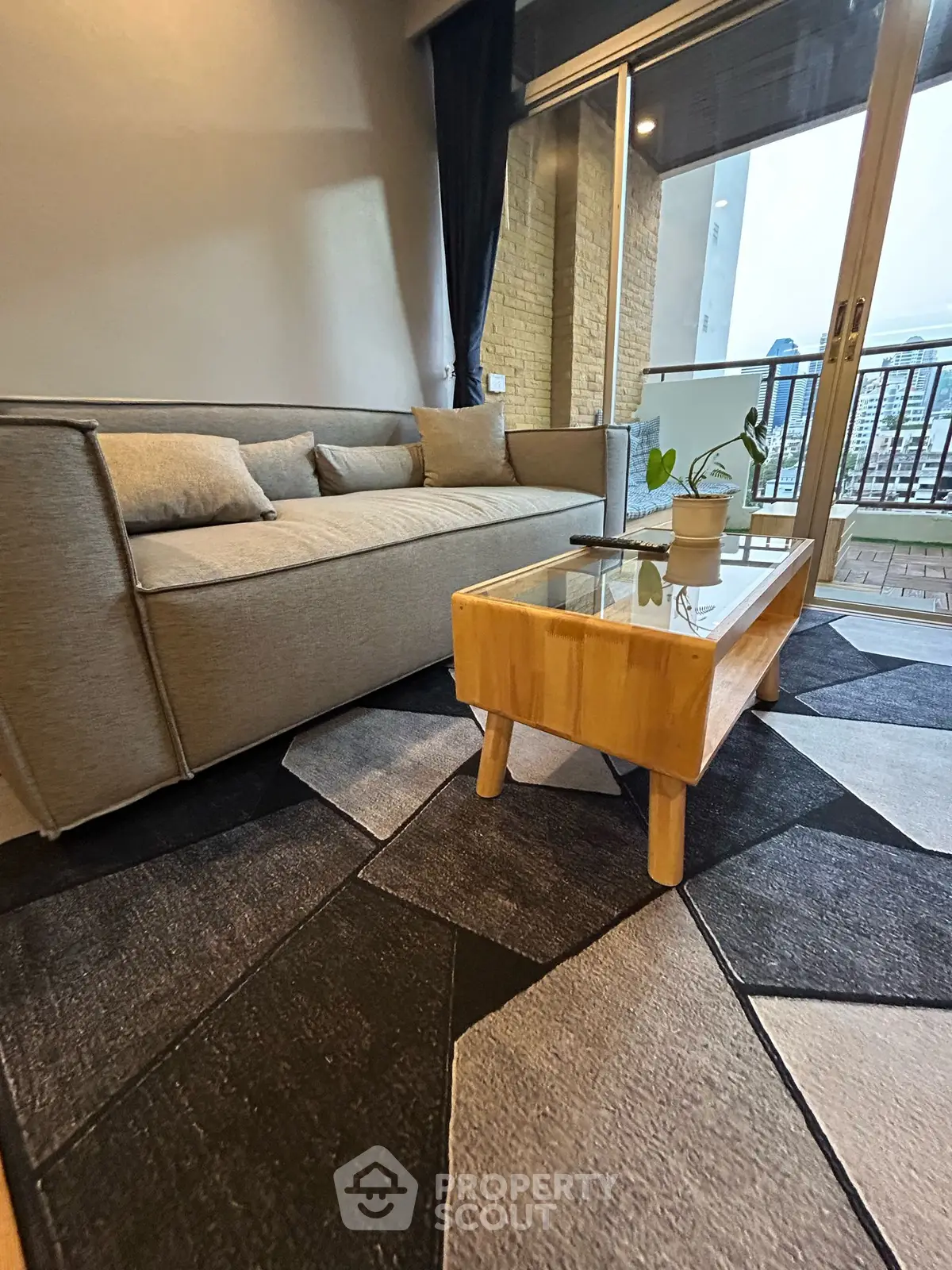 Stylish living room with modern sofa and glass coffee table, overlooking city view from balcony.