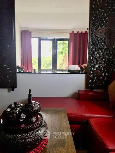 Charming living room with ornate decor and red accents, featuring a cozy seating area and large window with lush view.
