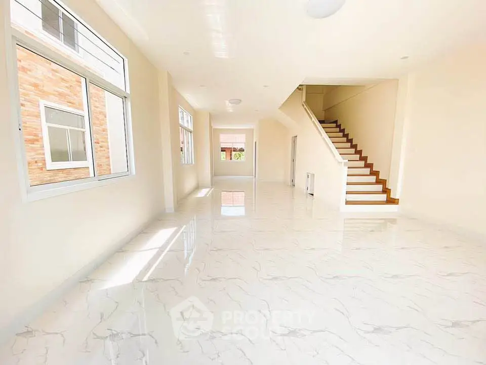 Spacious and bright open-plan living area with elegant staircase and large windows.