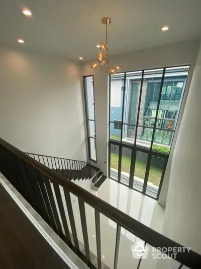 Elegant two-story home interior with modern staircase and chic gold chandelier, leading to a bright space with large windows and garden view.