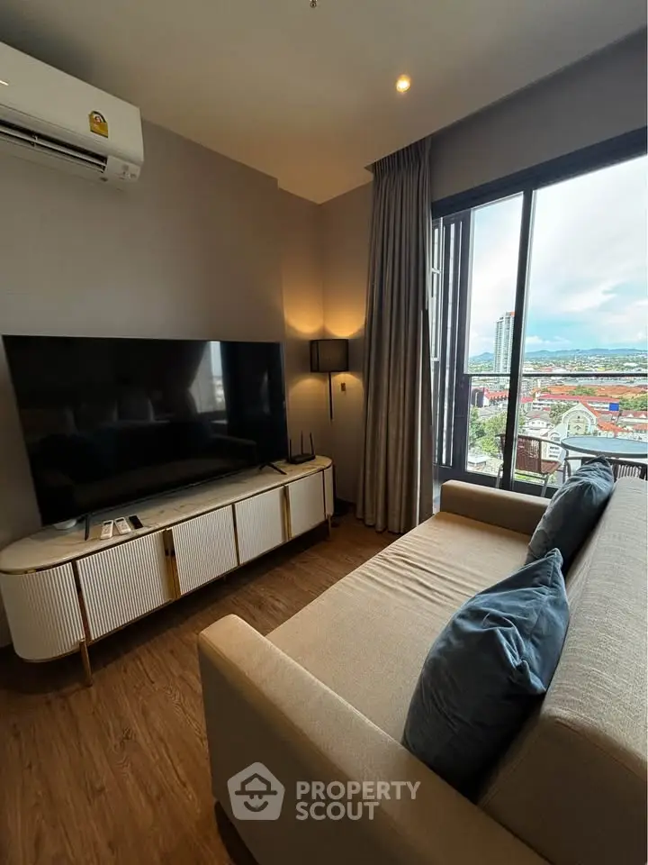 Modern living room with large TV, cozy sofa, and city view through window.