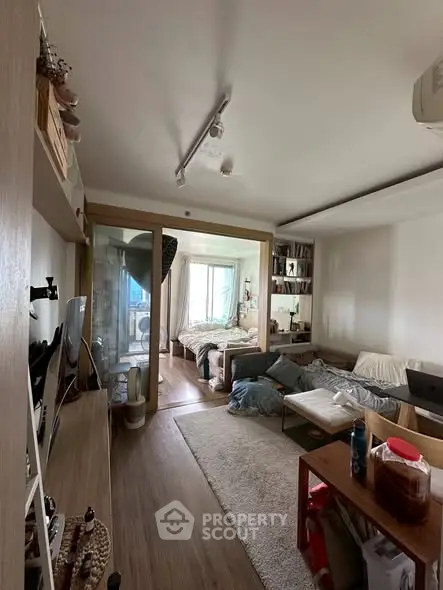 Cozy living room with wooden flooring and a view into a bedroom, featuring modern decor and ample natural light.