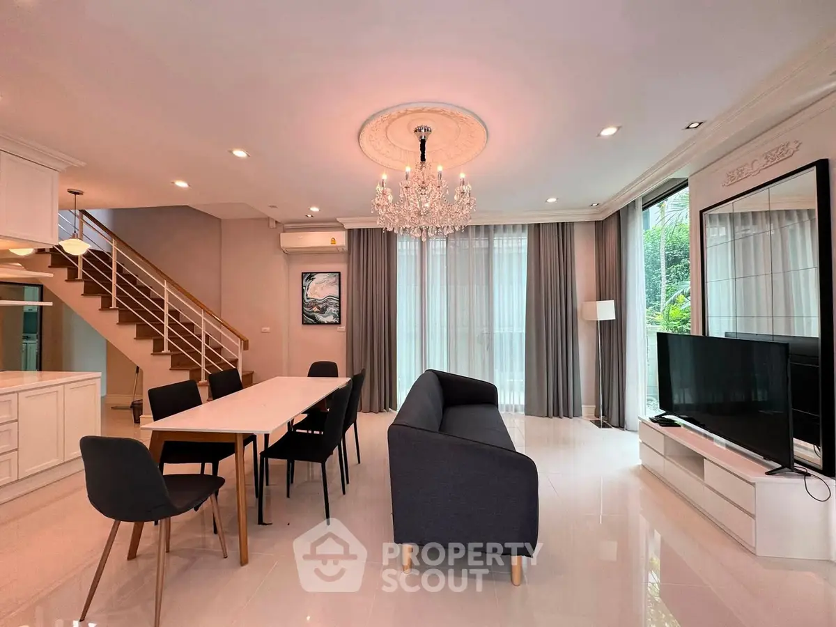 Elegant living room with chandelier, modern furniture, and open layout near staircase and large windows.