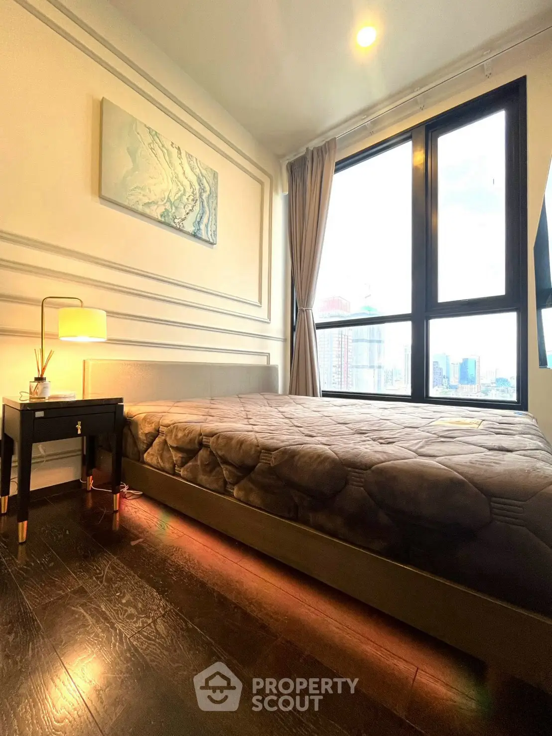 Modern bedroom with large windows and city view, featuring elegant decor and cozy lighting.