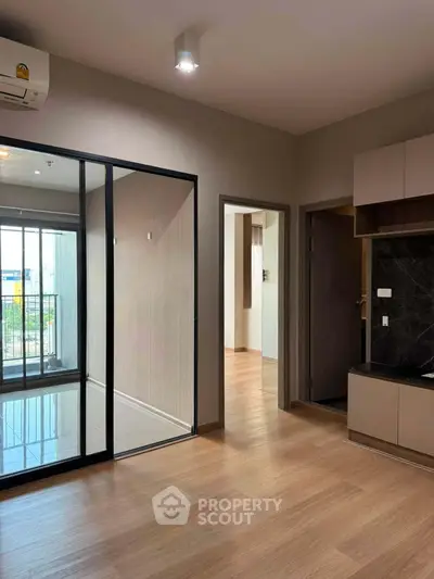 Modern apartment interior with wooden flooring and glass partition, featuring a compact kitchen area.