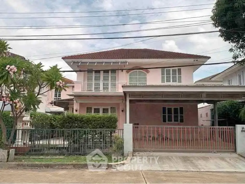 Charming two-story pink house with gated driveway and lush greenery