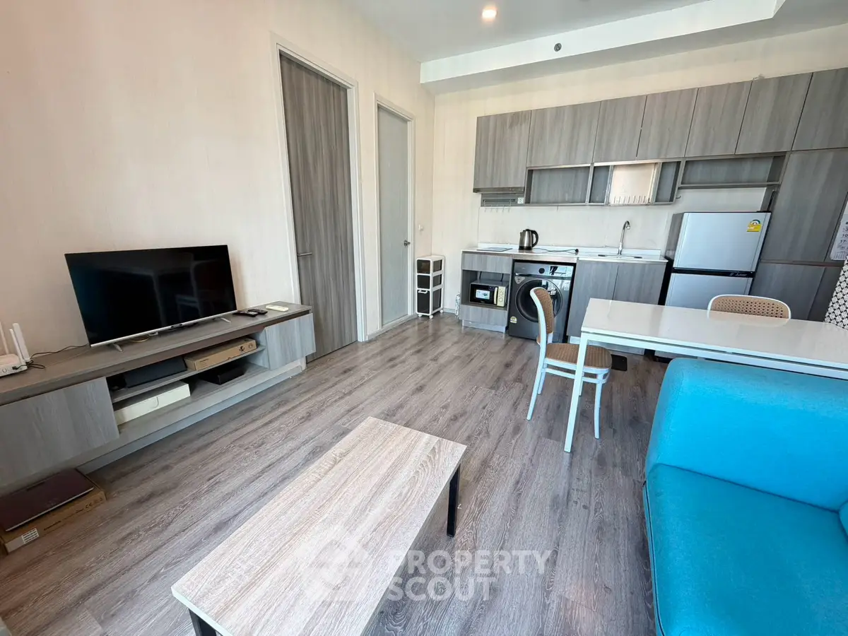 Modern open-layout living room with kitchen, featuring sleek furniture and appliances.