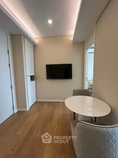 Modern living room with wooden flooring, wall-mounted TV, and cozy dining area.