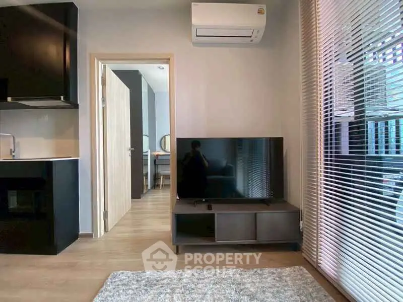 Modern living room with sleek design, featuring a TV, air conditioning, and open kitchen layout.