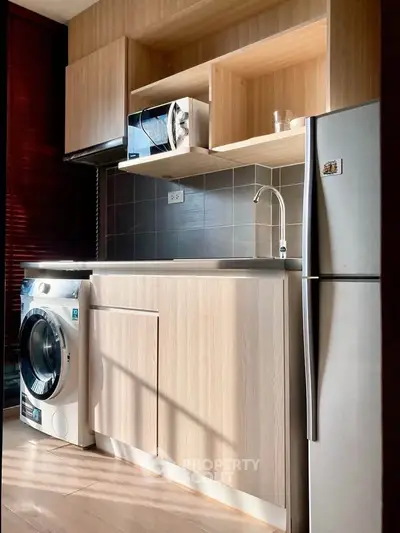 Modern kitchen with sleek appliances and wooden cabinetry, featuring a washing machine and fridge.