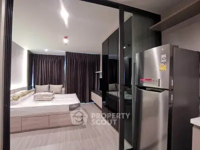 Modern studio apartment with sleek design, featuring a cozy bed, stylish cabinetry, and a stainless steel fridge.