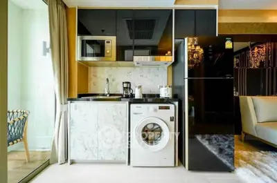 Modern kitchen with washing machine, microwave, and fridge in stylish apartment.