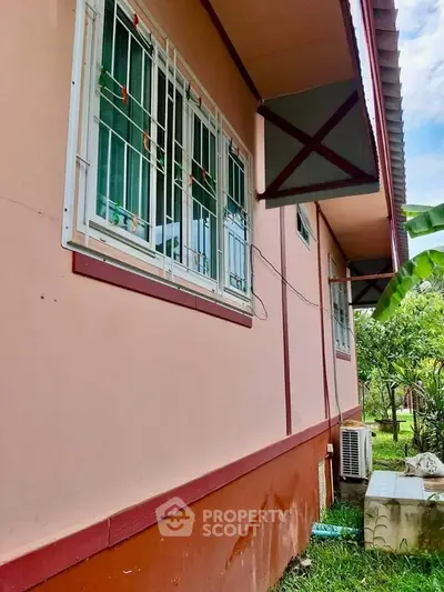Charming pink house exterior with lush greenery and secure window grills.
