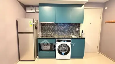 Modern kitchen with teal cabinets, washing machine, microwave, and fridge in compact layout.
