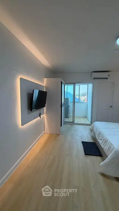 Modern bedroom with sleek TV setup and balcony access, featuring elegant wooden flooring and ambient lighting.