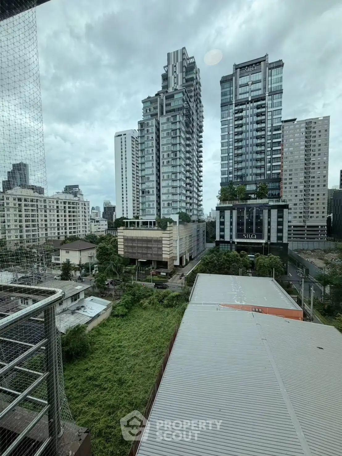 Stunning cityscape view from a high-rise balcony overlooking modern skyscrapers and lush greenery.