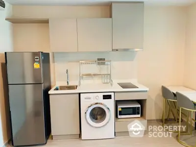 Modern compact kitchen with washing machine, fridge, and microwave in stylish apartment.