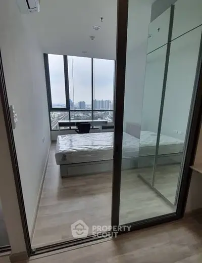 Modern bedroom with floor-to-ceiling windows offering stunning city views, featuring sleek mirrored closet doors.