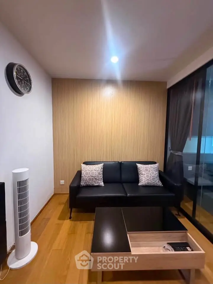 Modern living room with sleek black sofa, wooden flooring, and stylish decor in a cozy apartment.