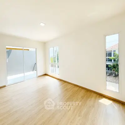 Spacious sunlit room with wooden flooring and large windows in modern home.