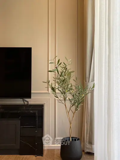 Elegant living room with modern TV setup and stylish potted plant, featuring chic wall paneling and natural light.