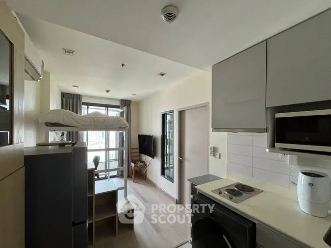 Modern studio apartment with integrated living space, featuring a sleek kitchen with built-in appliances, a cozy sleeping area, and ample natural light from the balcony doors.