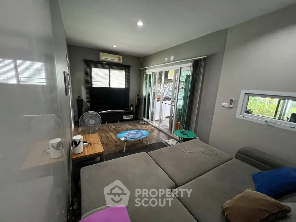 Modern living room with large sofa and entertainment center, featuring sliding glass doors to a balcony.