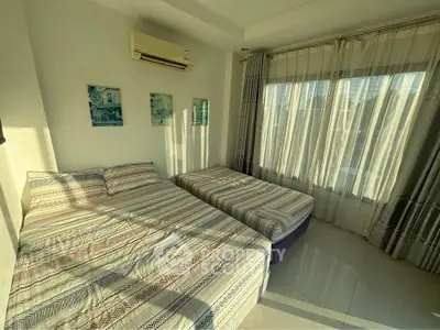 Bright bedroom with two beds and large window, featuring modern decor and air conditioning.