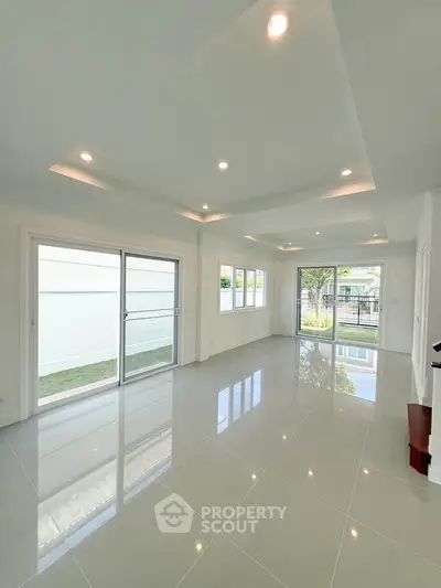 Spacious modern living room with large windows and glossy tiled floors, offering abundant natural light.