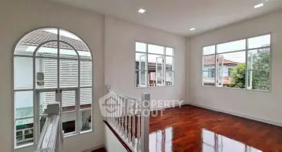 Spacious sunlit room with elegant wooden flooring and large windows in a modern home.