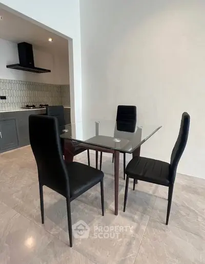 Modern dining area with glass table and sleek black chairs in open kitchen layout.
