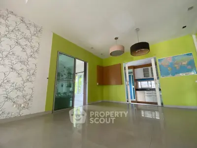 Spacious living room with vibrant green walls and modern lighting, adjacent to a kitchen area.