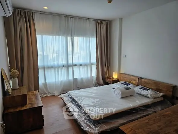 Cozy bedroom with wooden furniture and large window with sheer curtains.