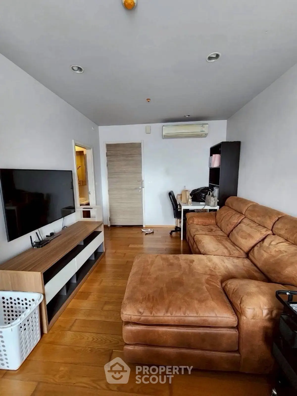 Spacious living room with modern furnishings and wooden flooring, featuring a large TV and comfortable sofa.