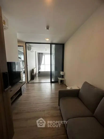 Modern living room with sleek design and glass partition, featuring cozy sofa and wooden flooring.