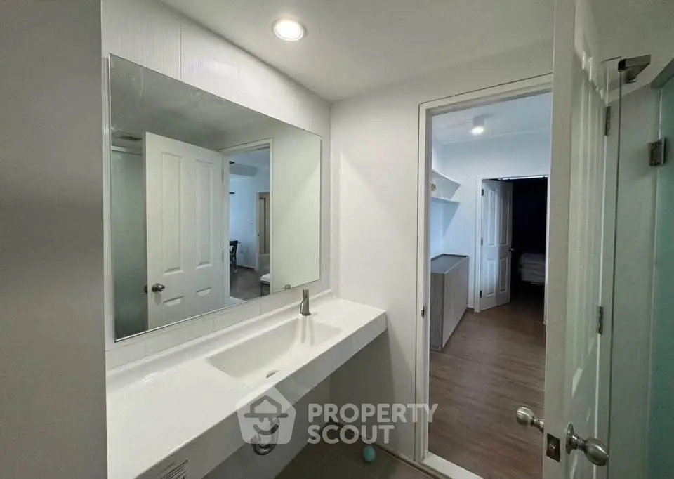 Modern bathroom with sleek sink and mirror, leading to a cozy bedroom with wooden flooring.