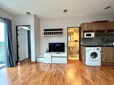 Modern open-plan living room with wooden flooring, TV, and kitchen appliances in a stylish apartment.