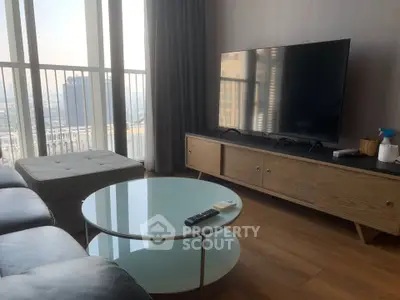 Modern living room with large TV, sleek furniture, and panoramic city view from high-rise apartment.