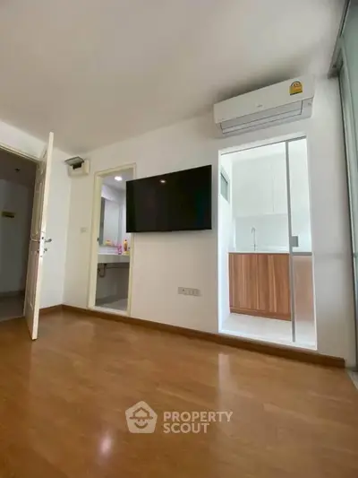 Modern apartment interior with wooden flooring, wall-mounted TV, and air conditioning unit.